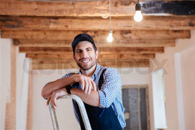 Smiling handyman standing on the ladder at the working area indoors, stock photo