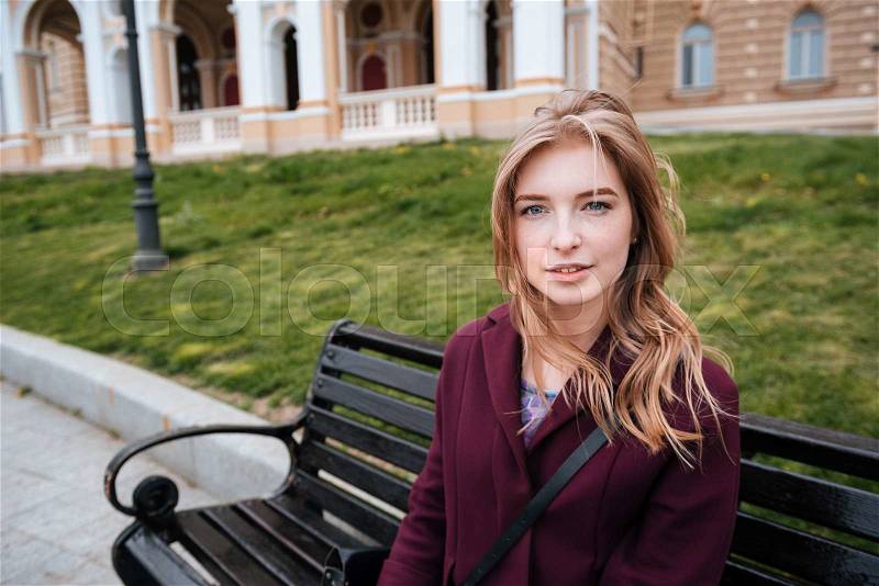 Portrait of cute lovely young woman sitting on bench outdoors, stock photo