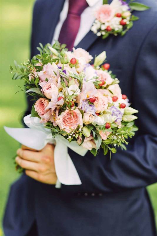 Male hands holding beautiful bridal bouquet with roses and red berries in summer, stock photo