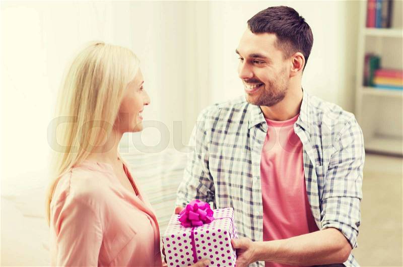 Relationships, love, people, birthday and holidays concept - happy man giving woman gift box at home, stock photo