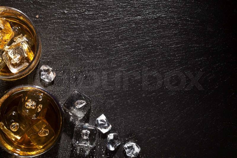 Glasses of whiskey with ice on black stone table. Top view with copy space, stock photo