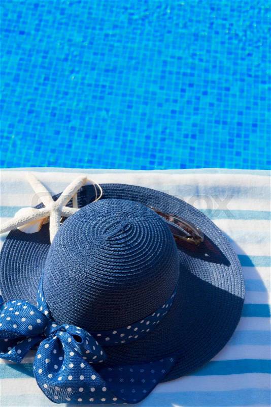 Towel and summer blue hat with seashells near pool, copy space on blue water, stock photo