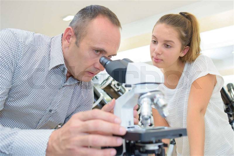 Man in shop looking in microscope, lady waiting, stock photo