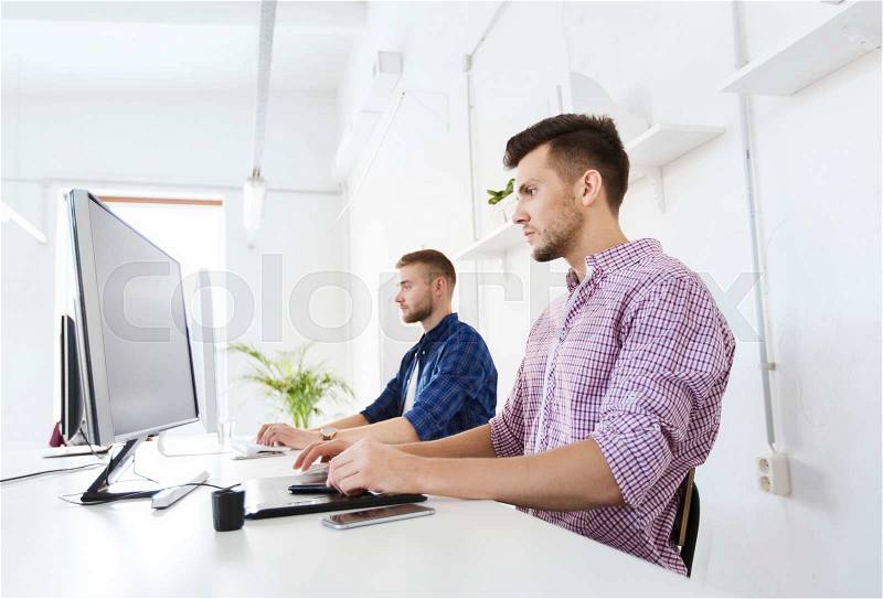 Business, technology, design and people concept - young creative man or designer with computer and pen tablet working at office, stock photo