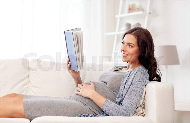 Pregnancy and motherhood concept - smiling pregnant woman lying on sofa and reading book, stock photo