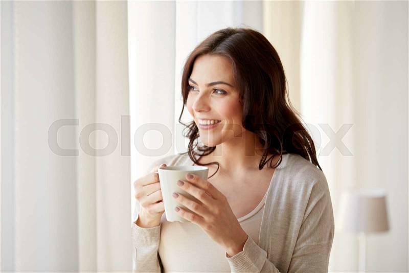 People, drinks and leisure concept - happy young woman with cup of tea or coffee at home, stock photo