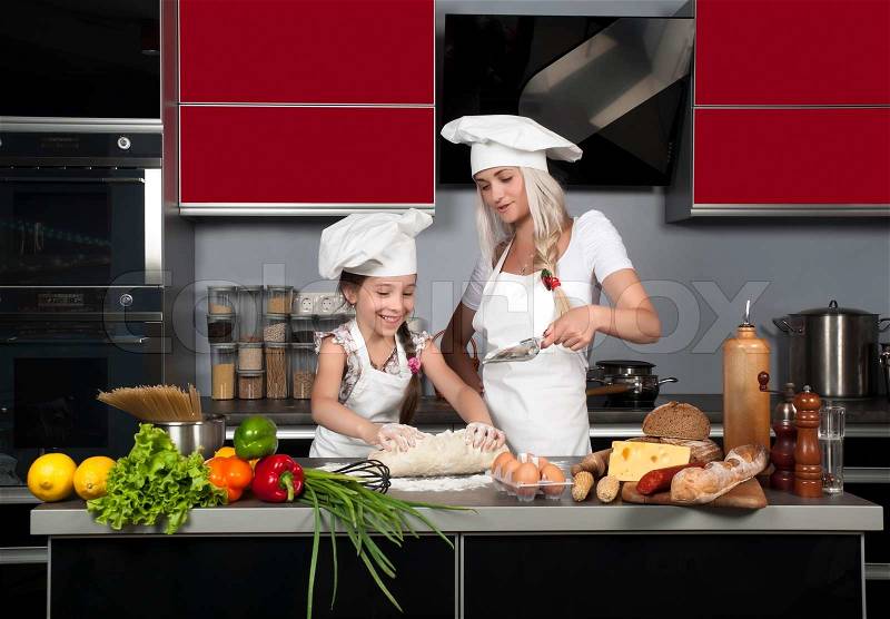 Mom teaches daughter to cook in the kitchen at the table with raw food, clothing cooks, stock photo