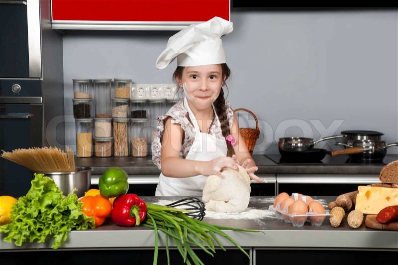Little girl chef knead the dough on the kitchen table with raw food, stock photo