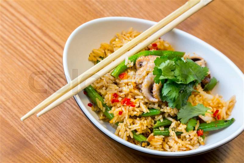 Asian riсe with seafood and vegetables in oval plate with bamboo sticks on a wooden table in asian restaurant, stock photo
