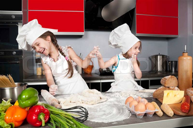 Two little girls having fun on the kitchen table with raw food, clothing cooks, stock photo