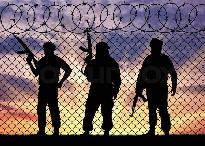 Concept of terrorism. Silhouette terrorists near the border fence in the background at sunset, stock photo