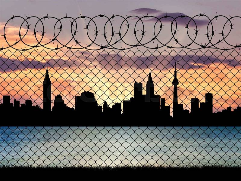 Concept of a border zone. Silhouette of the city behind a fence with barbed wire on a background of sunset and sea, stock photo