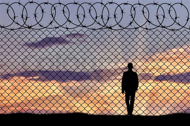 Concept of refugee. Silhouette of refugee near the border fence in the sunset, stock photo