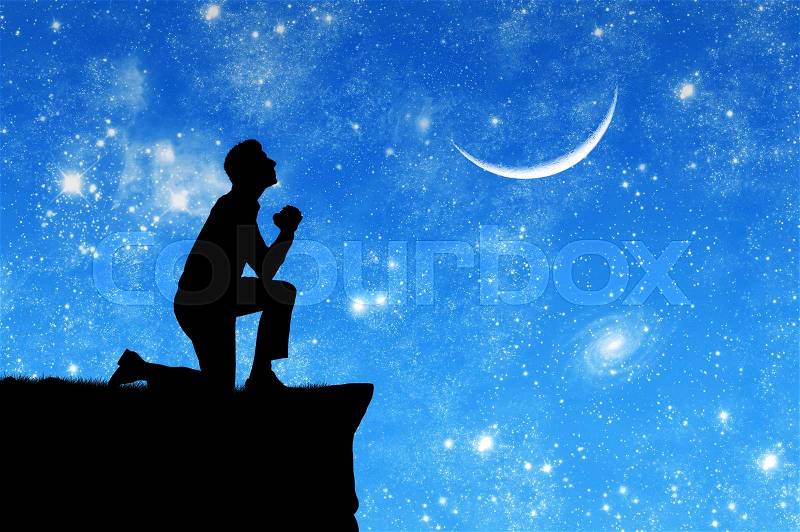 Concept of religion. Silhouette of man praying on the background of the sky with the moon and stars, stock photo