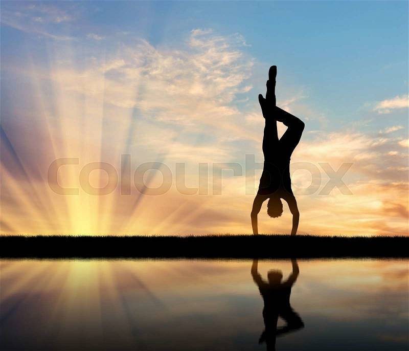 Concept of meditation and relaxation. Silhouette of a man practicing yoga at sunset and reflection in water, stock photo