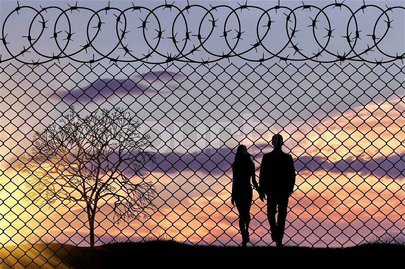 Concept of refugee. Silhouette family of refugees near the border fence in the sunset, stock photo