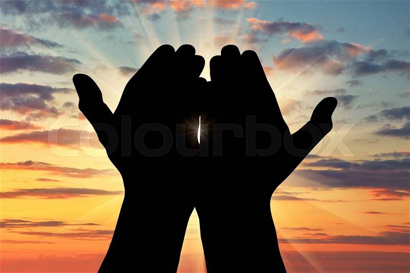 Сoncept of Islam, the Koran. Silhouette of praying hands facing the sky at sunset, stock photo