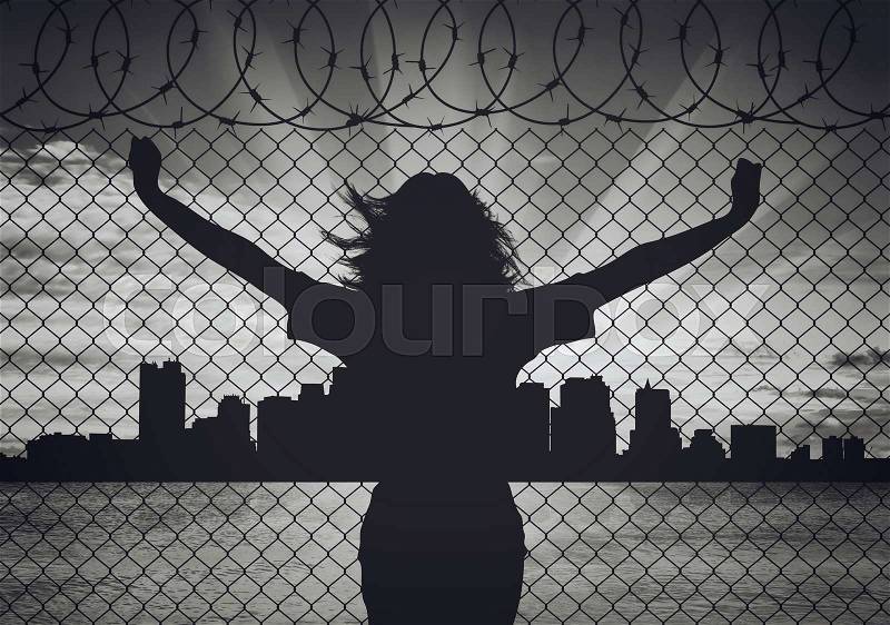 Concept of refugee. Silhouette of a woman refugee near the border on the background of the city in the distance, stock photo