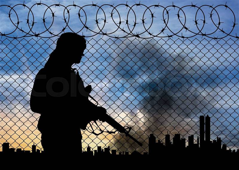 Concept of terrorism. Silhouette terrorists near the border fence in the background on the city in smoke at sunset, stock photo