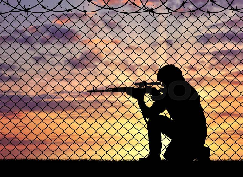 Concept of terrorism. Silhouette of a terrorist sniper near the border fence in the sunset, stock photo