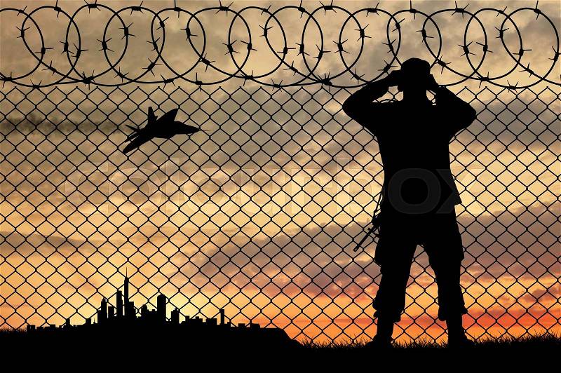 Concept of terrorism. Silhouette of a terrorist near the fence to follow the city at sunset, stock photo