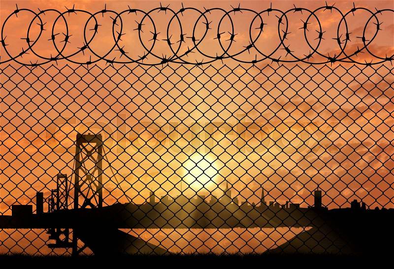 Concept of border service. Silhouette of a border fence with barbed wire on the background of the city at sunset, stock photo