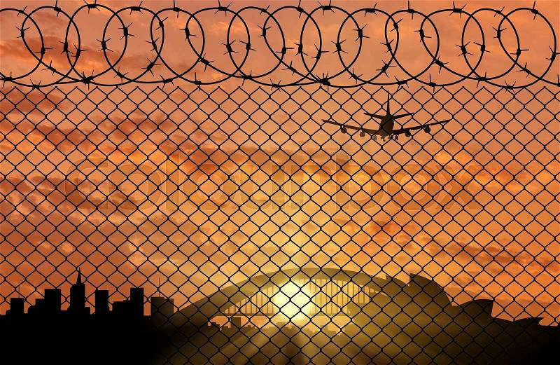 Concept of border service. Silhouette of a border fence with barbed wire on the background of the city at sunset, stock photo