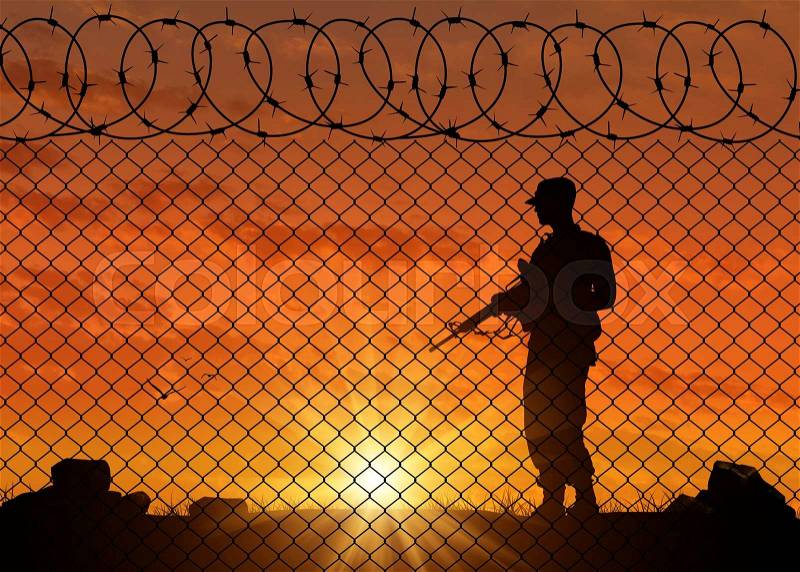 Concept of terrorism. Silhouette of a terrorist near the border fence in the sunset, stock photo