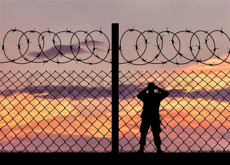 Concept of security. Silhouette of a military border guard and a fence on the background of sunset, stock photo