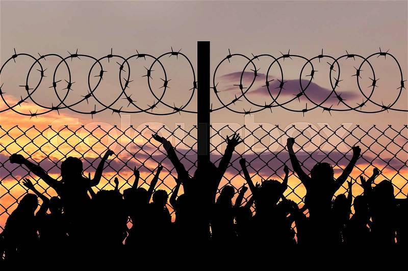 Concept of security. Silhouette of refugees climb over the barbed wire at the border, stock photo