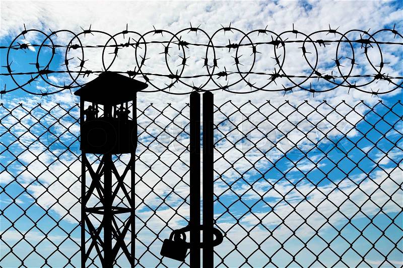 Silhouette of a watchtower and an iron fence with barbed wire on the cloudy sky, stock photo