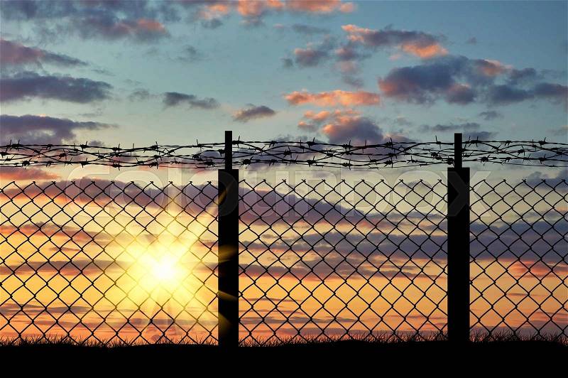 Boundary. Silhouette of iron fence with barbed wire on the background of sunset, stock photo