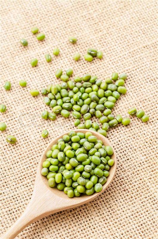 Healthy nutrition green raw organic mung beans in wooden spoon on vintage textile background, stock photo