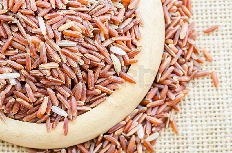 Red rice in a wooden dish on sack background, stock photo