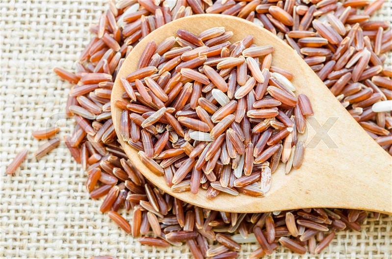 Red rice in a wooden spoon on sack background, stock photo