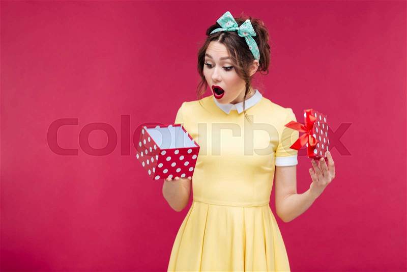 Wondered cute young woman opening gift box over pink background, stock photo