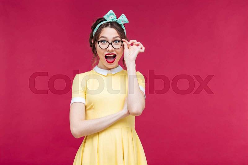 Happy attractive pinup girl in yellow dreass and glasses over pink background, stock photo