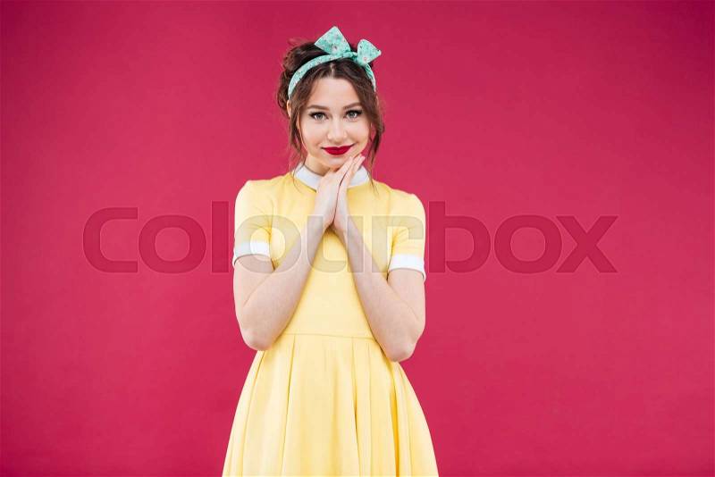 Happy beautiful pinup girl in yellow dress and headband over pink background, stock photo