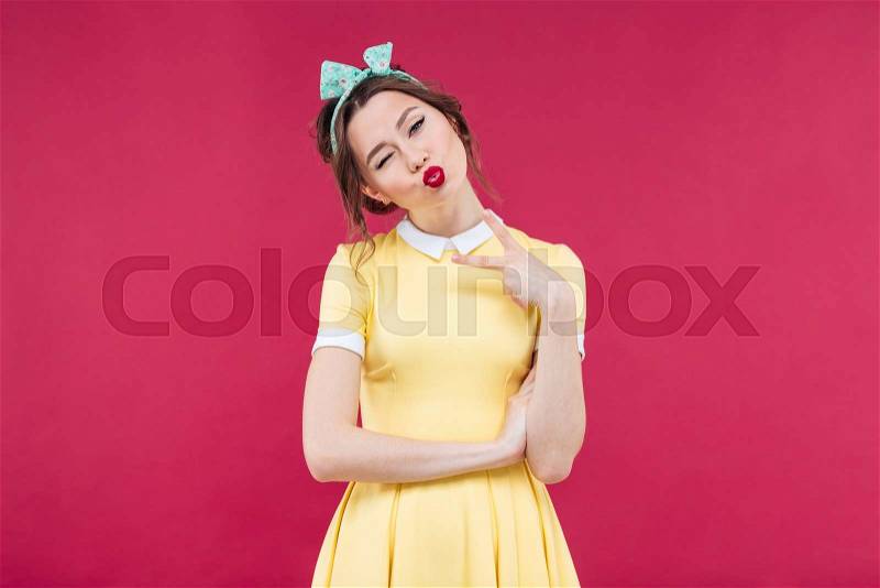 Pretty playful pinup girl winking and sending a kiss over pink background, stock photo
