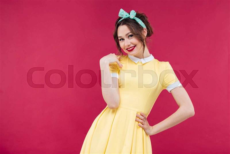 Smiling beautiful young woman in yellow dress standing over pink background, stock photo