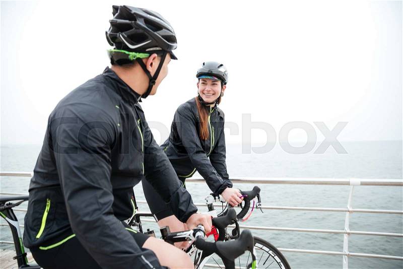 Smiling couple on bicycle resting and talking near sea, stock photo
