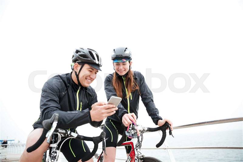 Smiling couple on bicycles resting and using smartphone together outdoors, stock photo