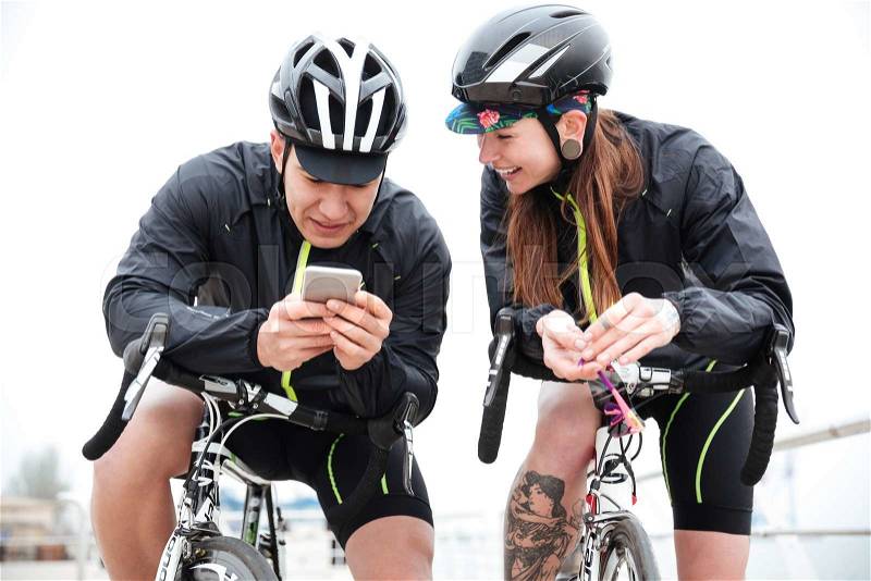 Happy couple on bicycles resting and using smartphone together outdoors, stock photo