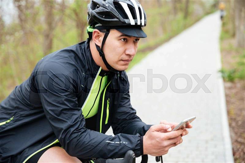 Serious young man in bike helmet with bicycle using cell phone, stock photo
