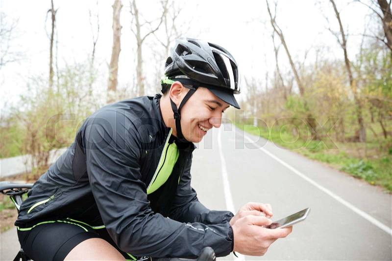 Serious young man in protective helmet with bicycle using cell phone, stock photo
