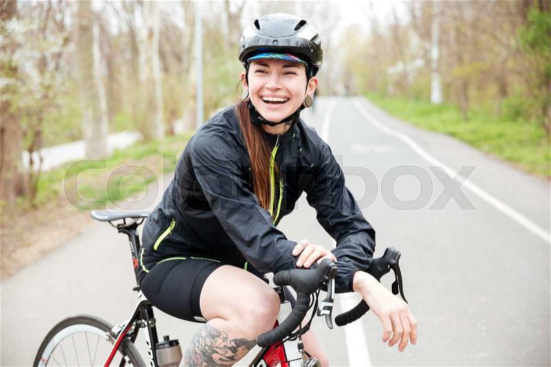 Happy beautiful young woman in bicycle helmet on bike standing on road and laughing, stock photo