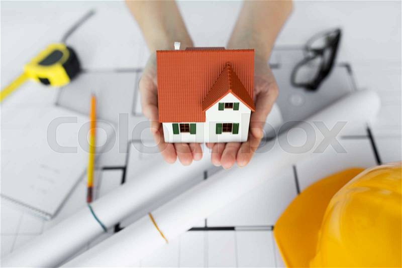 Architecture, building, construction, real estate and people concept - close up of architect hands holding living house model above blueprint on table, stock photo