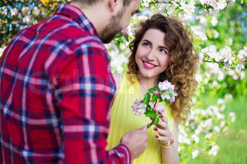 Young man giving flowers to happy girlfriend in summer garden, stock photo