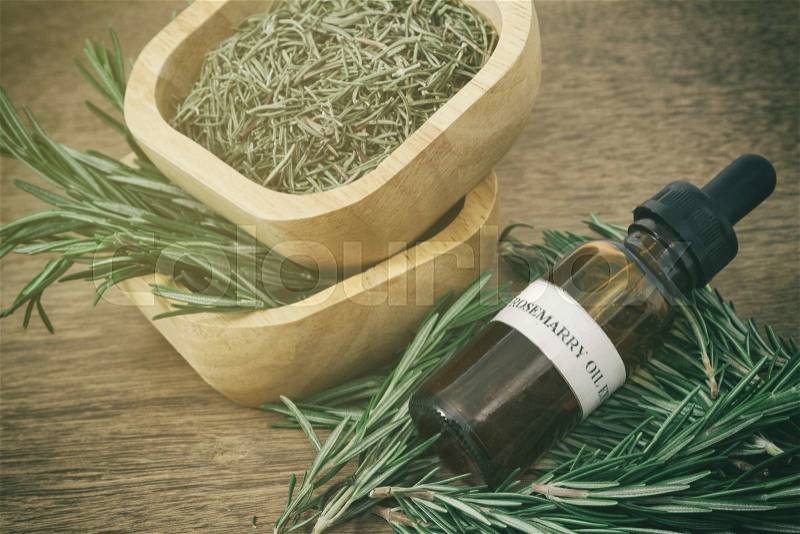 Rosemary essential oil in bottle and fresh rosemary on old wooden background, stock photo