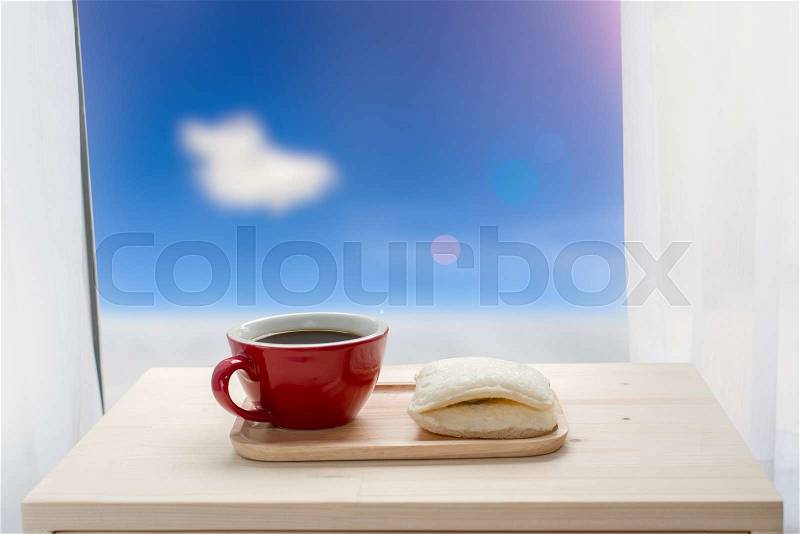 Red coffee cup and sandwich and window facing to snow, blue sky and len flare outside, stock photo
